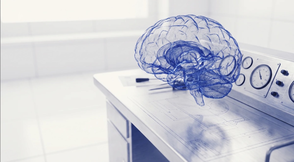 A wireframe model of a human brain resting on a laboratory desk covered in blueprints